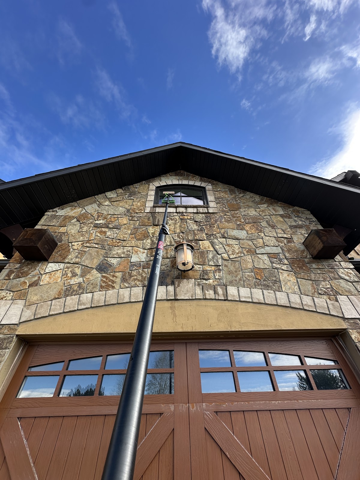 Water-fed pole reaching a peak window on a stone-facade Billings home
