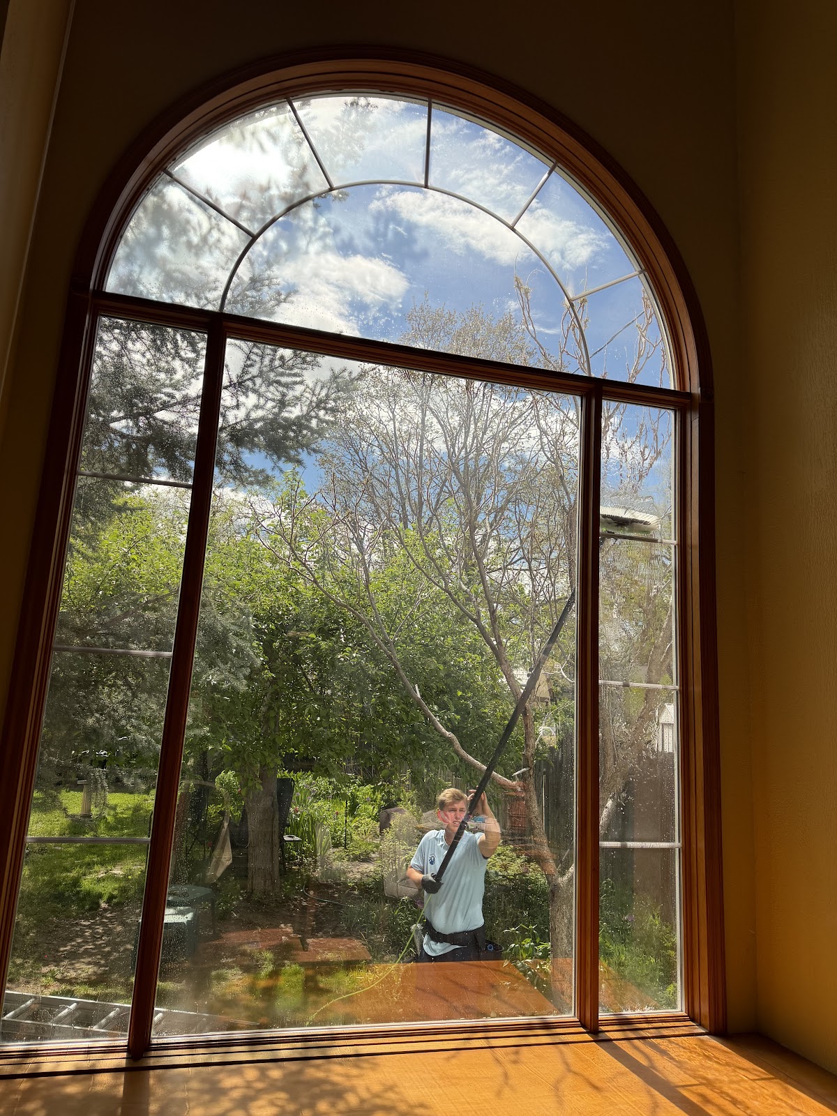 Crew member cleaning a large arched window seen from inside the home