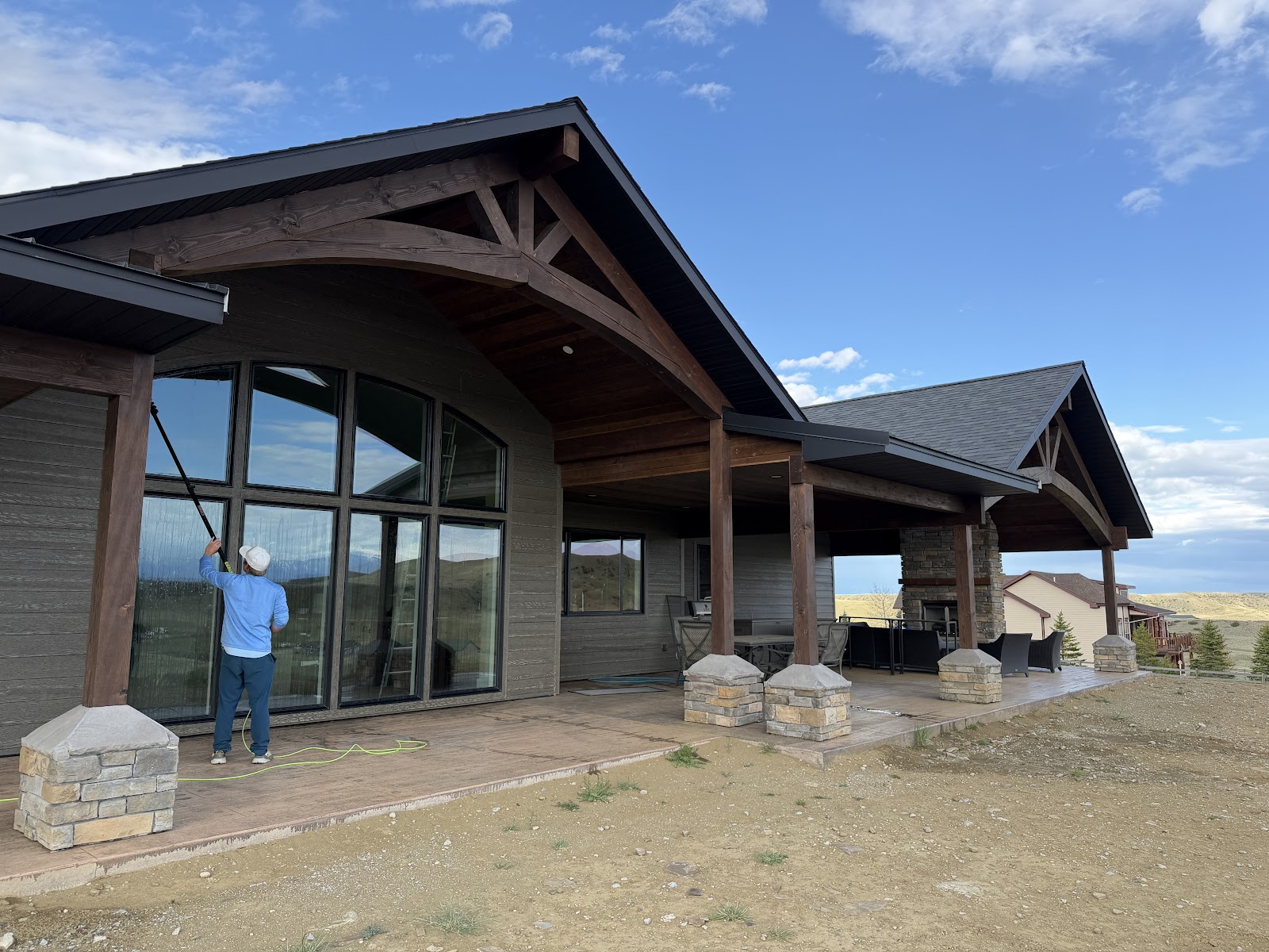 Scrub Squad technician cleaning a large arched window on a Montana mountain-view home